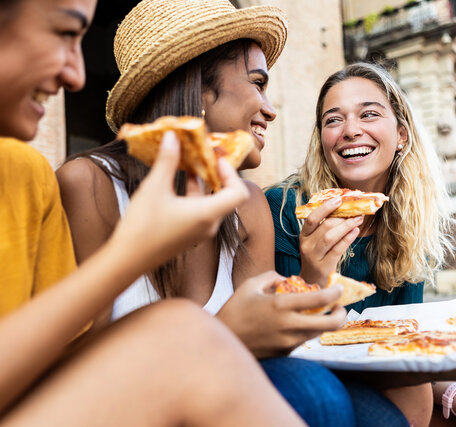 Drei junge Menschen essen Sommer auf einem Platz in Italien Pizza.