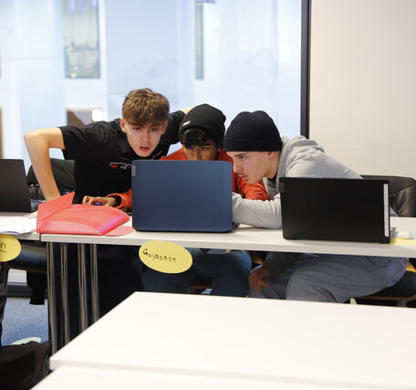 Drei Schüler der Informatikausbildung tauschen sich während einer Gruppenarbeit aus.